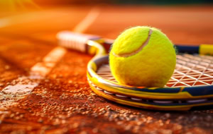 Tennisball auf einem Tennisschl&auml;ger auf einem Sandplatz bei Sonnenuntergang.