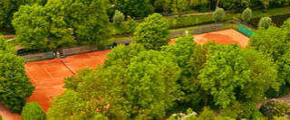 Luftaufnahme von zwei Tennispl&auml;tzen umgeben von B&auml;umen und Gr&uuml;nfl&auml;chen.