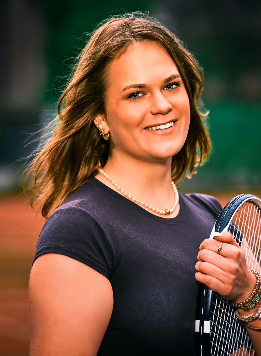 Frau mit Tennisschl&auml;ger auf einem Tennisplatz, l&auml;chelnd in die Kamera schauend.
