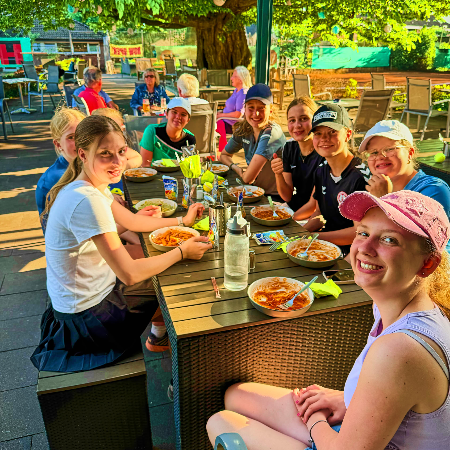 Eine Gruppe von Menschen sitzt an einem Tisch im Freien und isst.