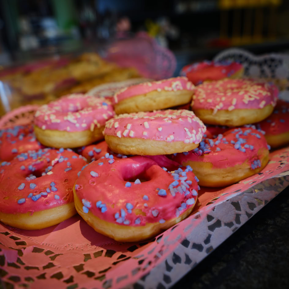 Ein Tablett mit mehreren Donuts, die rosa Zuckerguss und bunte Streusel haben.