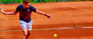 Ein Tennisspieler auf einem Sandplatz schl&auml;gt einen gelben Tennisball.