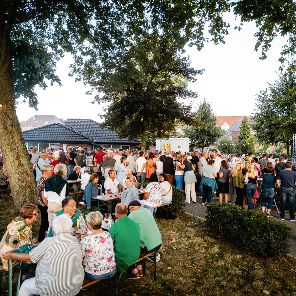 Menschenmenge auf einem Freiluftfest mit B&auml;umen und Zelten im Hintergrund.