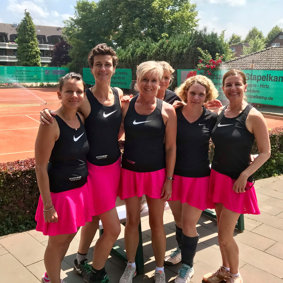 F&uuml;nf Personen in schwarzen Oberteilen und pinken R&ouml;cken stehen auf einem Tennisplatz.