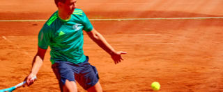 Ein Tennisspieler in gr&uuml;ner Kleidung schl&auml;gt einen gelben Ball auf einem Sandplatz.