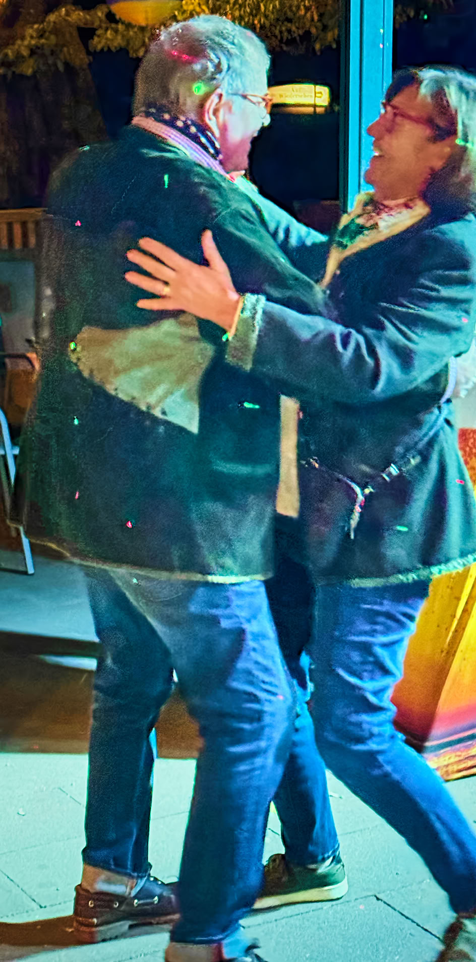 Zwei Personen tanzen zusammen im Freien, umgeben von beleuchteten Stehtischen.