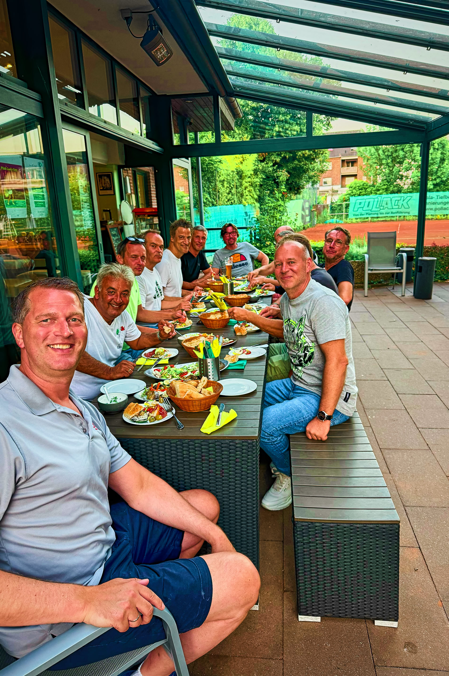 Eine Gruppe von Menschen sitzt an einem langen Tisch im Freien und isst gemeinsam.