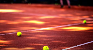 Mehrere gelbe Tennisb&auml;lle liegen auf einem Sandplatz mit wei&szlig;en Linien.