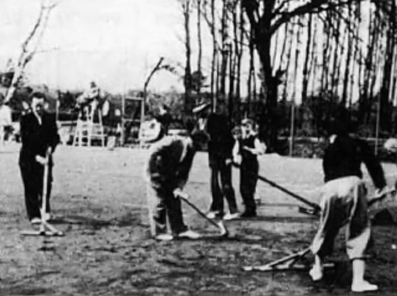 Vier Personen in Tennisbekleidung stehen auf einem Tennisplatz und halten Tennisschl&auml;ger.