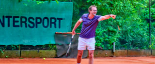 Ein Tennisspieler in lila Shirt und wei&szlig;en Shorts schl&auml;gt einen Ball auf einem Sandplatz. Im Hintergrund ist ein gr&uuml;nes Banner mit der Aufschrift "INTERSPORT" zu sehen.