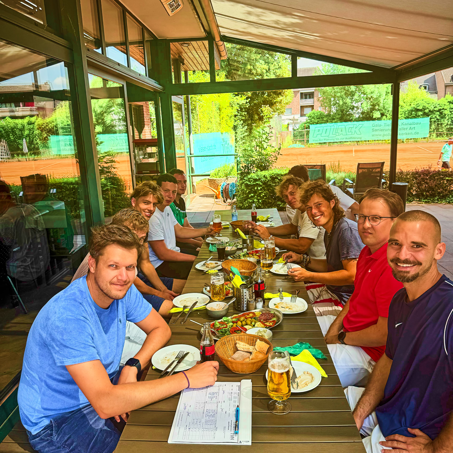 Eine Gruppe von Menschen sitzt an einem langen Tisch im Freien und isst gemeinsam.