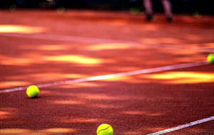 Tennisb&auml;lle auf einem Sandplatz mit wei&szlig;en Linien und Schatten.