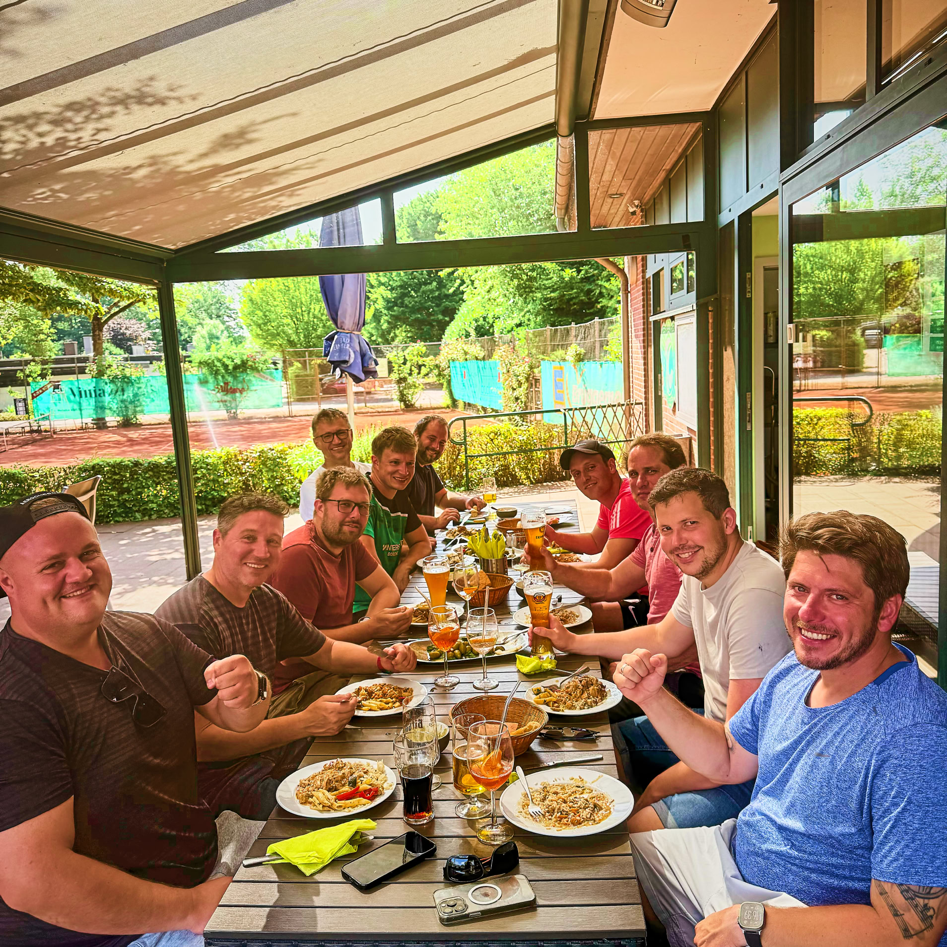 Eine Gruppe von Menschen sitzt an einem langen Tisch im Freien und isst.